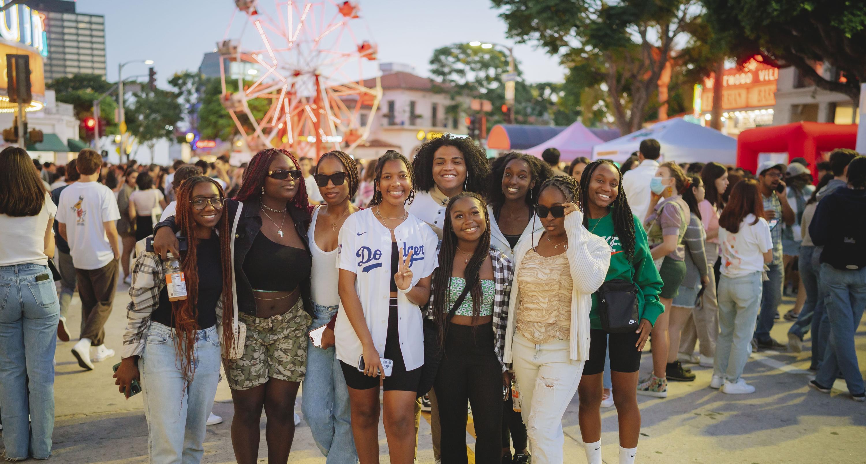 Group of students at the Block Party with vendors and guests around them and a ferris wheel in the distance.
