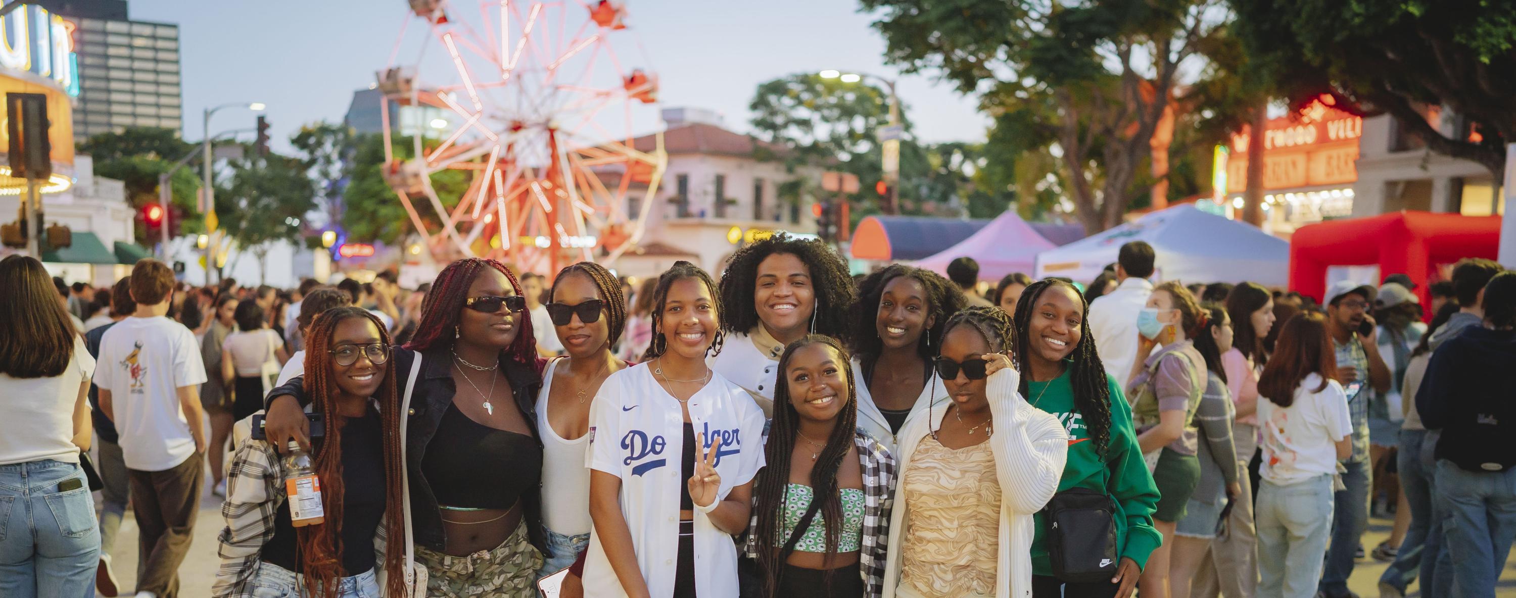 Group of students at the Block Party with vendors and guests around them and a ferris wheel in the distance.